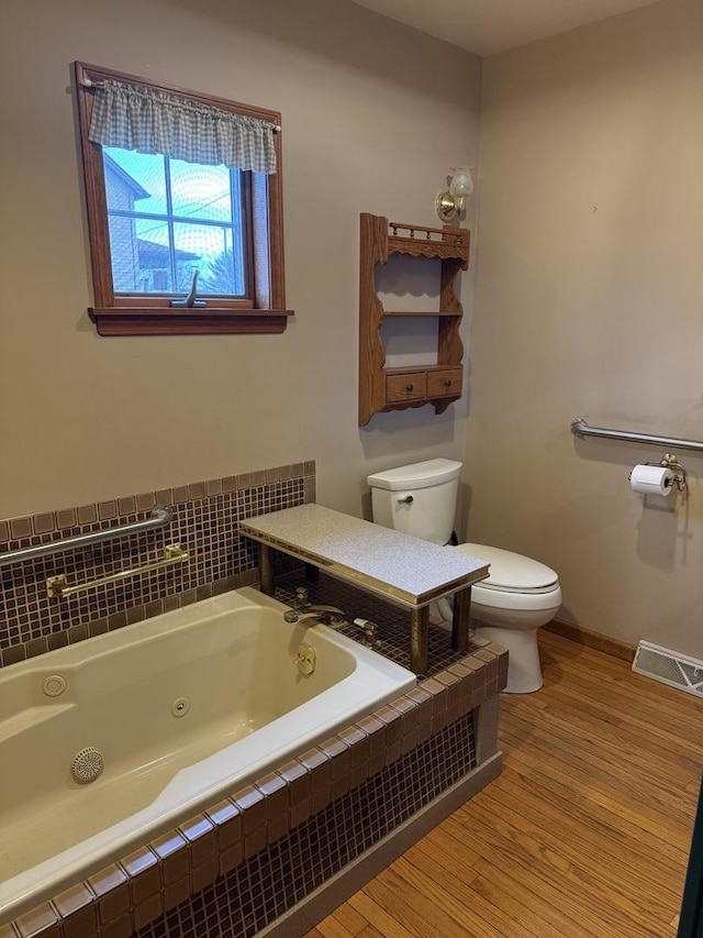 full bath featuring visible vents, toilet, wood finished floors, a whirlpool tub, and baseboards