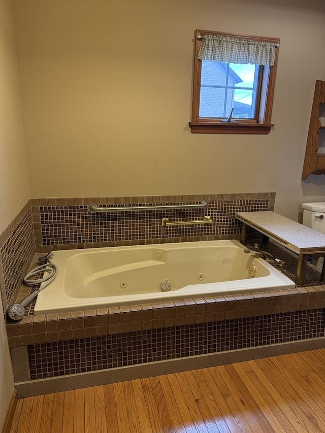 full bathroom featuring toilet, a tub with jets, and wood finished floors