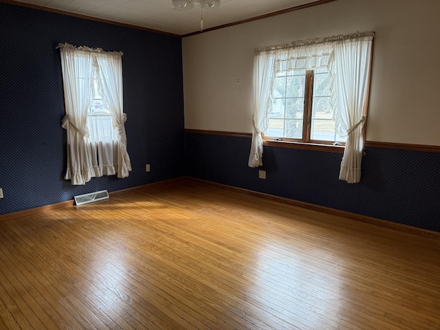 spare room featuring baseboards, visible vents, hardwood / wood-style floors, and ornamental molding