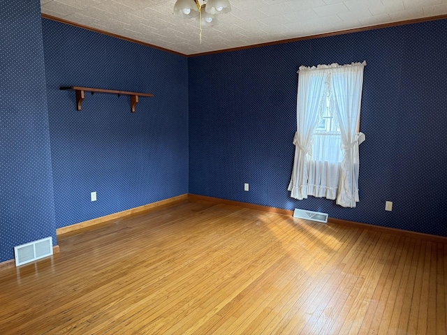 empty room featuring hardwood / wood-style floors, ornamental molding, and visible vents