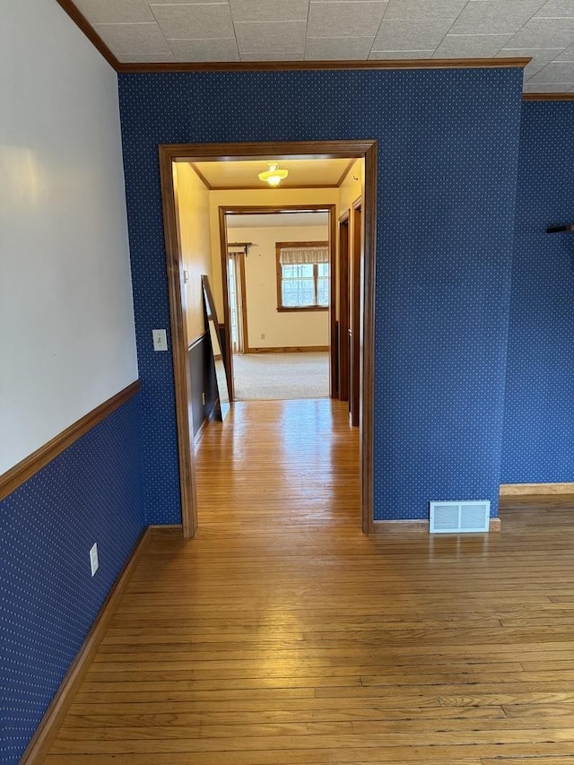 hall with light wood-style flooring, visible vents, ornamental molding, wainscoting, and wallpapered walls