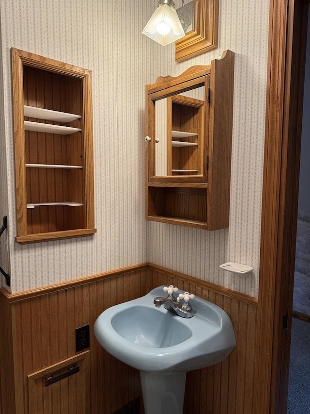 bathroom featuring a sink, wallpapered walls, and a wainscoted wall