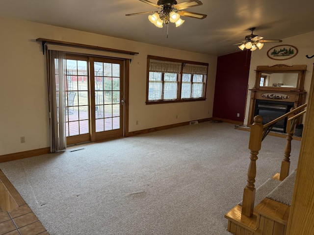 unfurnished living room featuring a glass covered fireplace, light colored carpet, visible vents, and baseboards