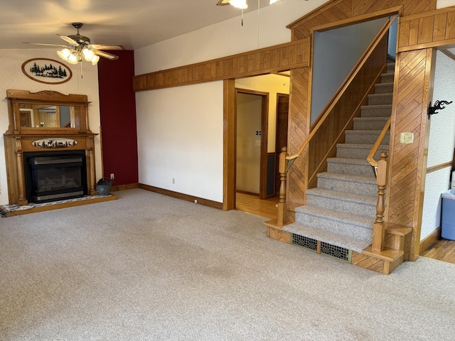 unfurnished living room with carpet floors, a glass covered fireplace, ceiling fan, and wood walls