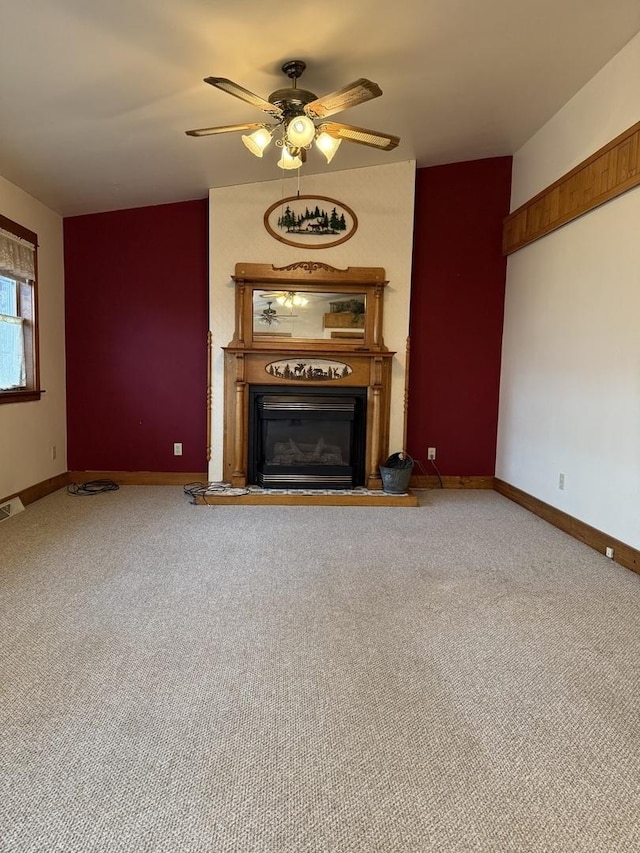 unfurnished living room featuring carpet flooring, a glass covered fireplace, a ceiling fan, and baseboards