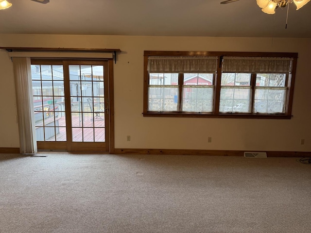 carpeted empty room with visible vents, ceiling fan, and baseboards