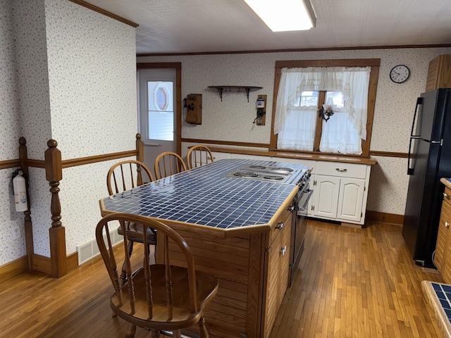 kitchen with tile countertops, wallpapered walls, a wainscoted wall, and freestanding refrigerator