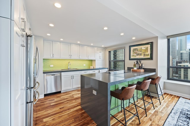 kitchen with stainless steel appliances, a peninsula, white cabinetry, a kitchen breakfast bar, and dark countertops