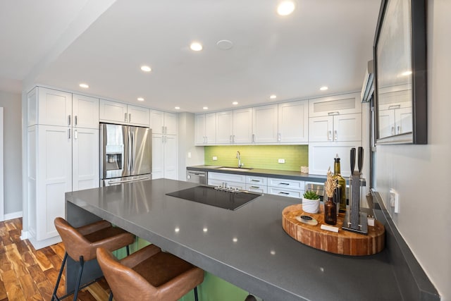 kitchen featuring stainless steel appliances, dark countertops, a sink, wood finished floors, and a kitchen breakfast bar