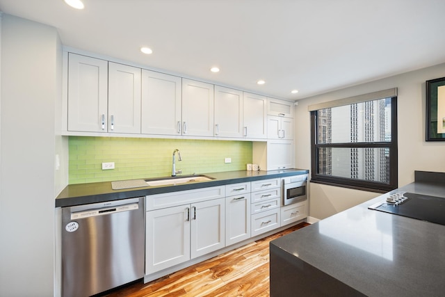 kitchen with black electric cooktop, a sink, white cabinets, dishwasher, and dark countertops