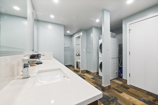 bathroom with stacked washer / drying machine, a sink, recessed lighting, and wood finished floors