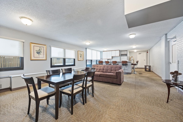 dining room featuring a textured ceiling, brick wall, and light colored carpet