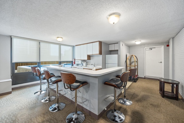 kitchen with light countertops, a breakfast bar, carpet floors, and freestanding refrigerator