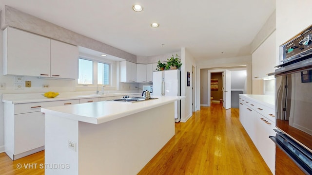 kitchen with light wood-type flooring, a sink, oven, and white cabinets