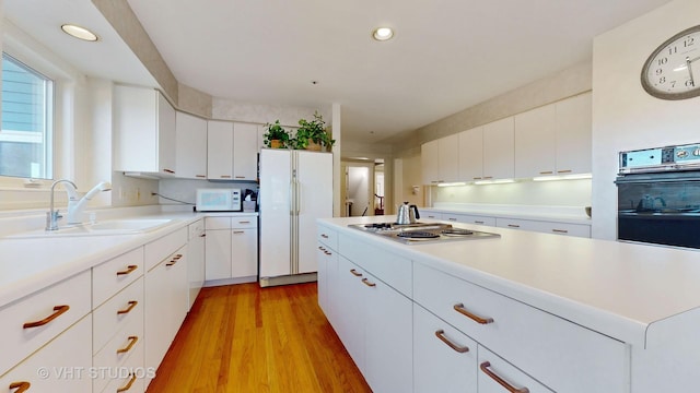 kitchen with light wood finished floors, light countertops, white cabinets, a sink, and white appliances