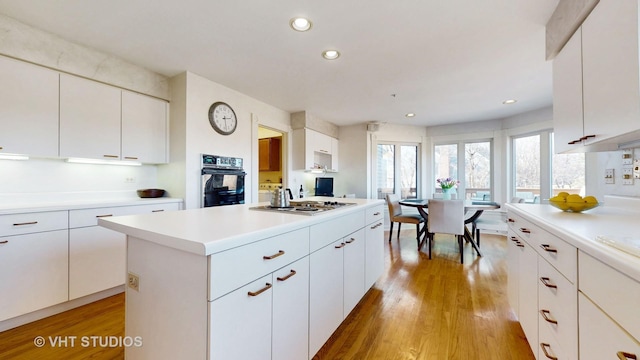 kitchen featuring light countertops, black oven, a kitchen island, and light wood finished floors