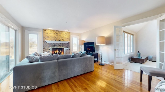 living room with light wood-style floors, a brick fireplace, french doors, and plenty of natural light