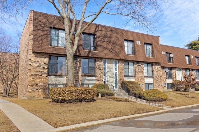 view of property featuring roof with shingles, brick siding, and mansard roof