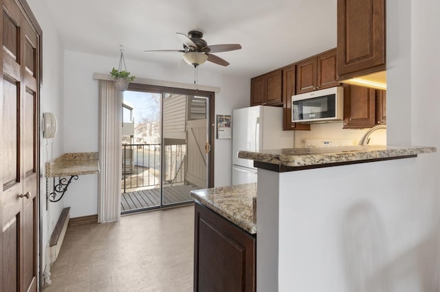 kitchen featuring ceiling fan, light stone counters, freestanding refrigerator, a peninsula, and light floors