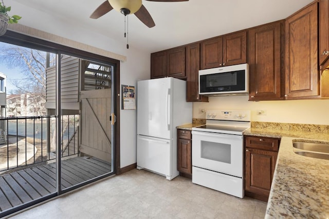 kitchen featuring white appliances, a sink, a ceiling fan, light stone countertops, and light floors