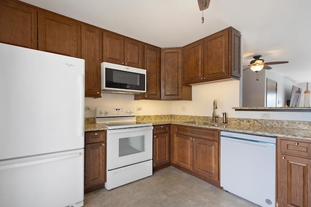 kitchen with light stone counters, white appliances, a sink, a ceiling fan, and brown cabinetry