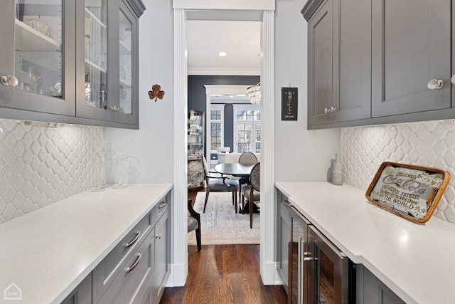 bar with beverage cooler, dark wood-type flooring, decorative backsplash, and crown molding