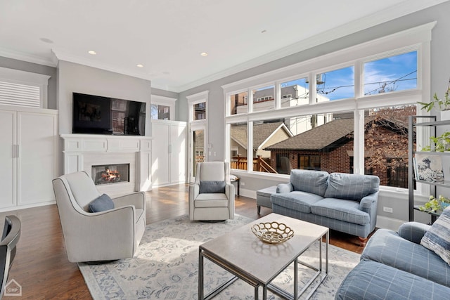 living area with recessed lighting, wood finished floors, baseboards, a glass covered fireplace, and crown molding