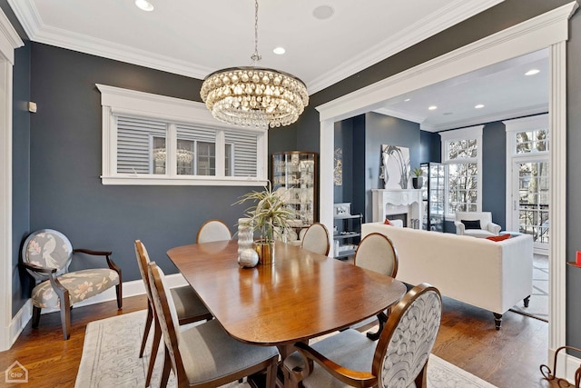 dining room with a chandelier, a fireplace, wood finished floors, baseboards, and crown molding