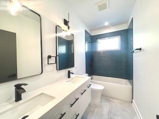 bathroom with toilet, visible vents, tub / shower combination, and a sink