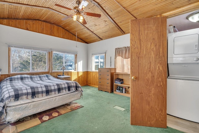 bedroom with stacked washer / drying machine, lofted ceiling, light colored carpet, wainscoting, and wooden ceiling