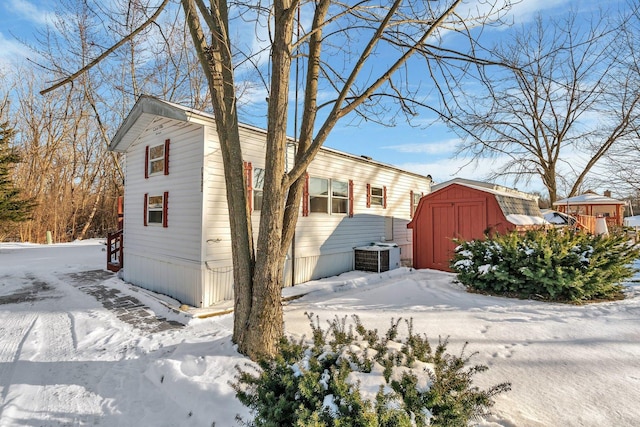 view of snowy exterior featuring a storage shed, cooling unit, and an outdoor structure