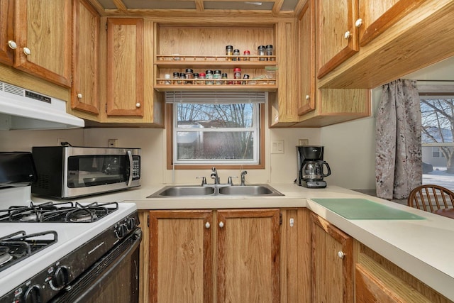 kitchen with under cabinet range hood, gas range gas stove, a sink, light countertops, and stainless steel microwave