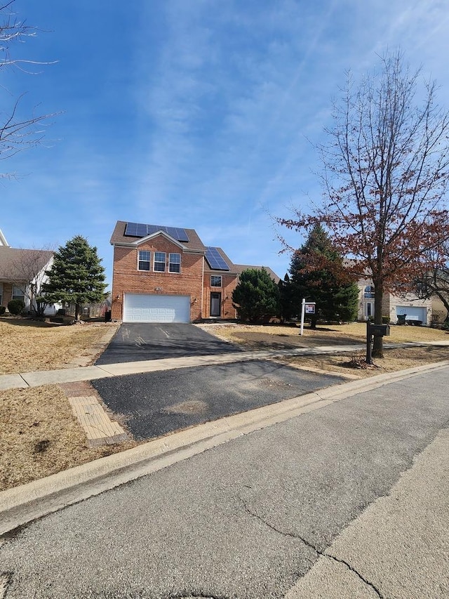 view of front of house with solar panels, brick siding, a garage, and driveway