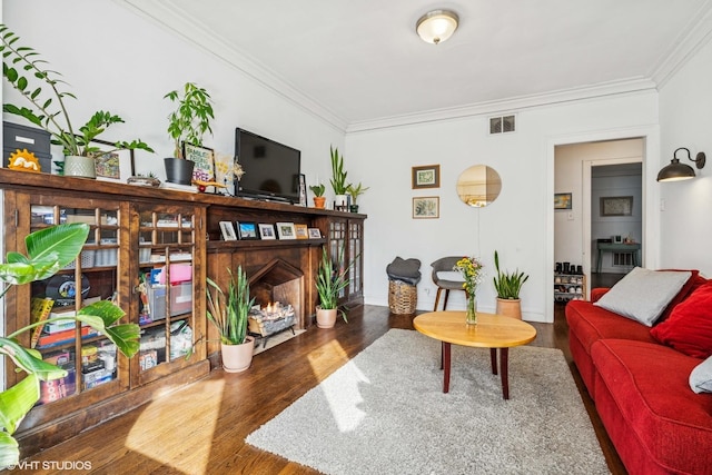 living area with ornamental molding, wood finished floors, visible vents, and a lit fireplace