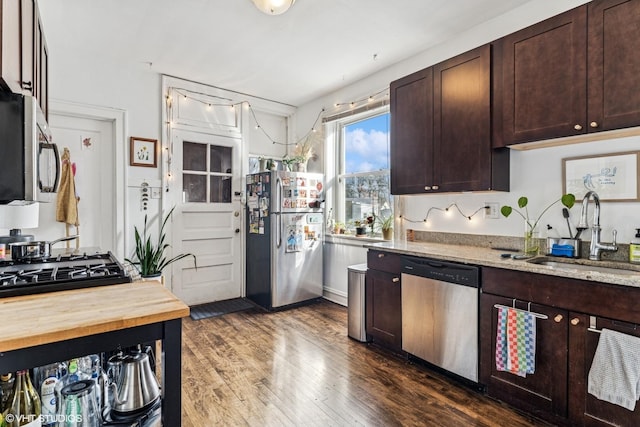 kitchen with a sink, dark wood-style floors, dark brown cabinetry, appliances with stainless steel finishes, and light stone countertops