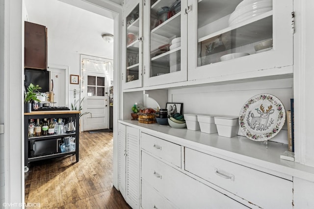 interior space featuring light countertops, white cabinets, wood finished floors, and glass insert cabinets