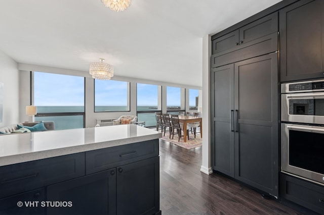 kitchen with dark wood-style flooring, a notable chandelier, light countertops, double oven, and open floor plan