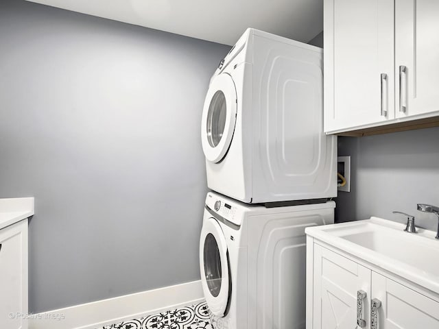 clothes washing area with stacked washer and dryer, cabinet space, a sink, and baseboards