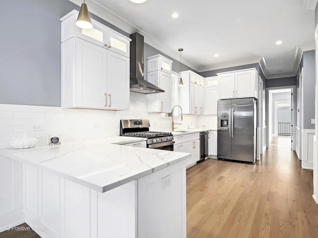 kitchen with appliances with stainless steel finishes, hanging light fixtures, wall chimney range hood, and a peninsula