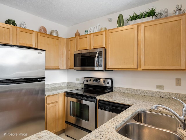 kitchen with a textured ceiling, light brown cabinetry, appliances with stainless steel finishes, and a sink