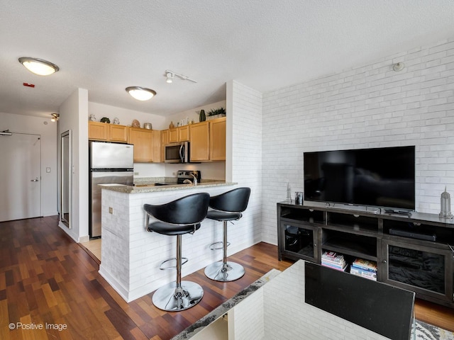 kitchen featuring a peninsula, stainless steel appliances, dark wood-type flooring, a textured ceiling, and a kitchen breakfast bar