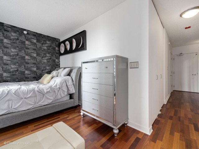 bedroom with an accent wall, wood finished floors, and baseboards