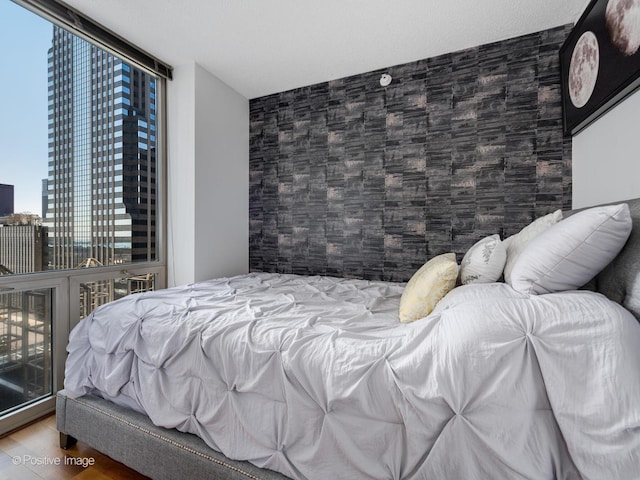 bedroom featuring expansive windows, a view of city, wood finished floors, and an accent wall