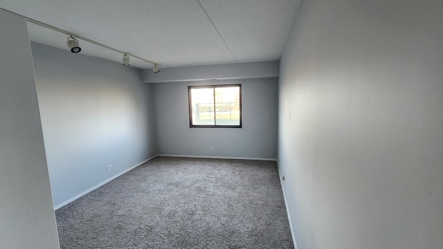 carpeted empty room featuring track lighting, a textured ceiling, and baseboards