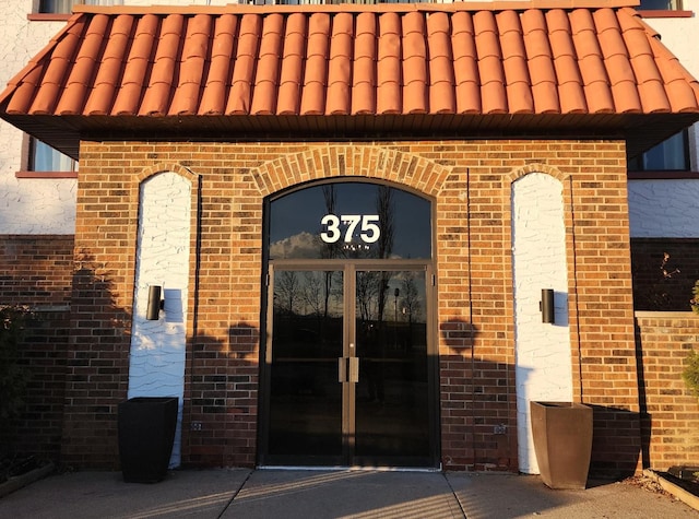 view of exterior entry with french doors, brick siding, and a tiled roof