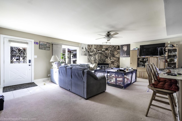 living area with a ceiling fan, light carpet, light tile patterned flooring, a stone fireplace, and baseboards