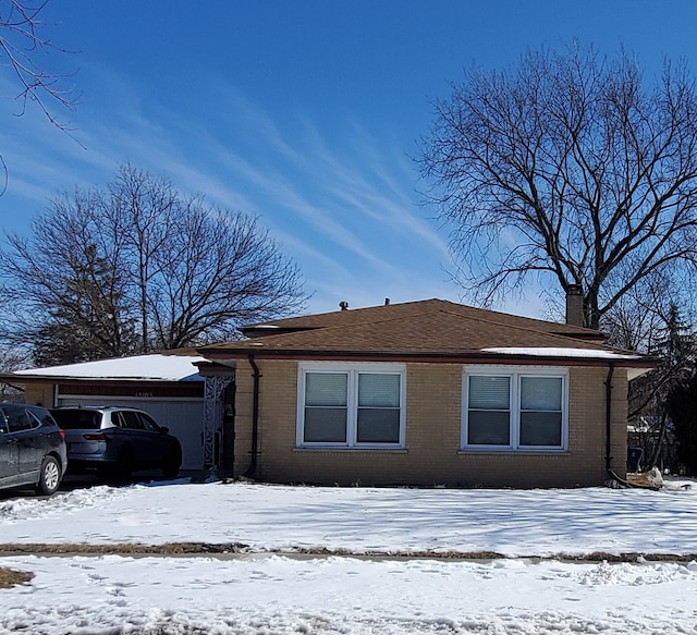 view of snowy exterior featuring brick siding, a chimney, and an attached garage