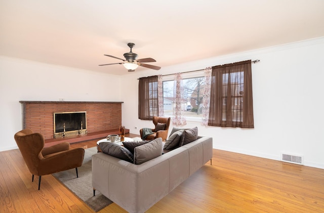 living room featuring light wood-type flooring, a fireplace, visible vents, and crown molding