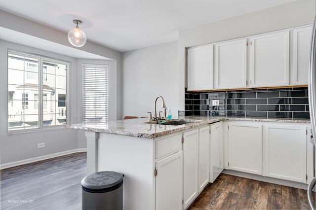 kitchen featuring a peninsula, white cabinets, backsplash, light stone countertops, and dark wood finished floors