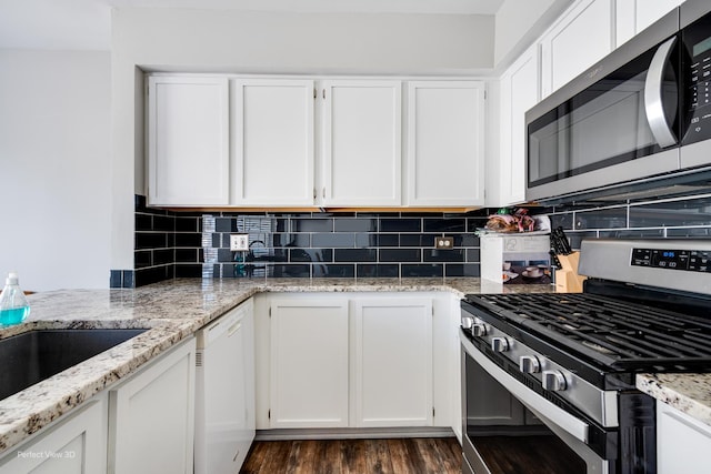 kitchen with white cabinets, light stone counters, stainless steel appliances, and backsplash